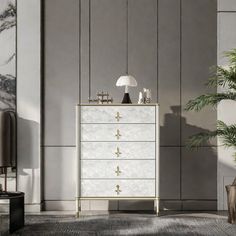 a white and gold chest of drawers next to a plant in a room with grey walls