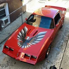 a red car with an eagle painted on it's hood parked in front of a fence