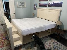 a dog sitting on the floor in front of a bed with a mattress and drawers