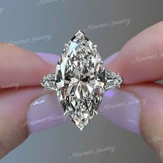 a person's hand holding a fancy ring with a large diamond in the center