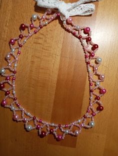 a pink and white beaded necklace on a wooden floor with a string attached to it