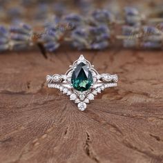 an engagement ring with a green stone surrounded by white diamonds on a piece of wood