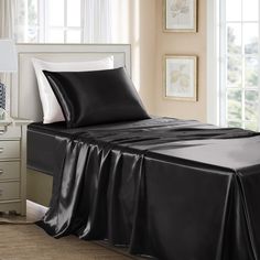 a bed with black sheets and pillows in a room next to a dresser, lamp and window