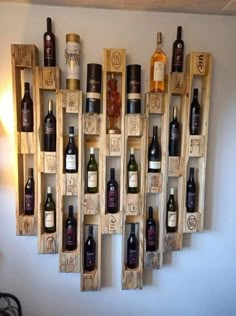 wine bottles are arranged on wooden crates in the shape of a wall hanging from a white wall