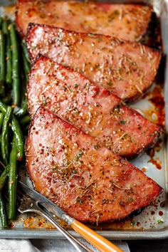 some meat and green beans are on a tray with silverware next to it,