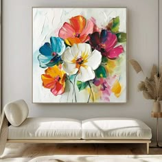 a white couch sitting under a painting on the wall next to a vase filled with flowers