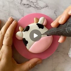 someone is decorating a cow cake with icing and a sharpie knife on a pink plate