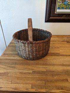 a basket sitting on top of a wooden table next to a framed painting in a frame