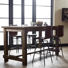 a dining table with four chairs and a potted plant on it in front of large windows