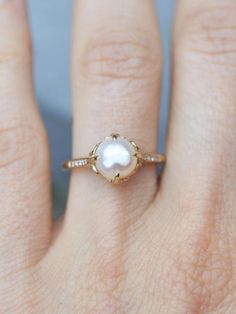 a woman's hand with a gold ring and a white pearl on the middle