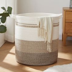 a white and brown basket sitting on top of a wooden floor next to a plant