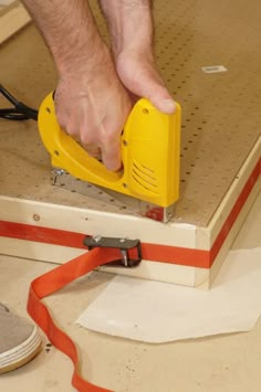 a man is using a sanding machine on a piece of wood with red tape