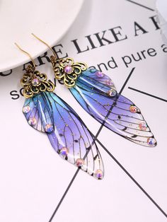 the blue and purple butterfly earrings are on top of a table next to a plate