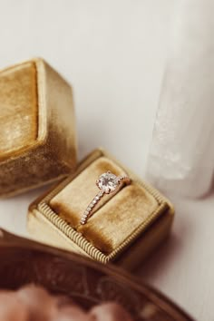 an engagement ring sits in a velvet box on a table next to two other gold boxes