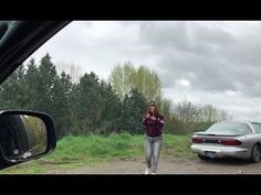 a woman walking down a dirt road next to a car