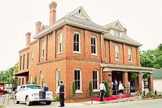 an old brick building with cars parked in front and people walking around the street outside