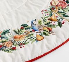 an embroidered table runner with birds and flowers on it, along with red trimming