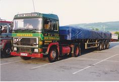 a green and red truck with a tarp on it's flatbed in a parking lot