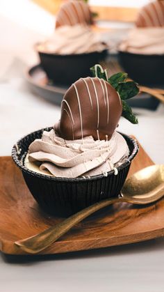 a chocolate cupcake on a wooden plate with a gold spoon and two other desserts in the background