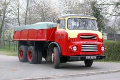 an old red and yellow dump truck driving down the road with trees in the background