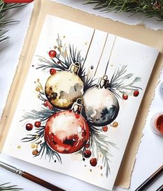 watercolor christmas ornament painting on white paper surrounded by paintbrushes and other art supplies