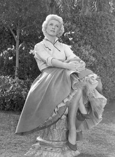 an old photo of a woman sitting on top of a tree stump with her legs crossed