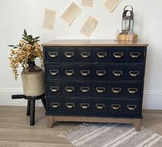 a black dresser with lots of drawers next to a lamp and flowers on the table