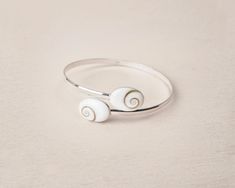 Our 925 Sterling silver delicate bracelet is perfect for elegant ocasions. This unique design consists in two stones of Santa Lucia 14 mm in oval shape, a natural shell also know as Shiva Eye Shell. The shiva shell is a natural fossil seashell. This piece is fully adjustable, able to wear it on the up side of the arm or on the wirst. This delicate bracelet is the a perfect present for all those who loves the sea and natural beauty. Details: - 925 Sterling Silver Stamp - Able for sensitive skins. Minimalist White Sterling Silver Bangle Bracelet, Minimalist White Sterling Silver Bangle, Adjustable Minimalist Sterling Silver Bracelet, White Sterling Silver Oyster Bangle Bracelet, White Sterling Silver Bangle Bracelet, Handmade Sterling Silver Bracelet In White, Handmade White Sterling Silver Bangle Bracelet, Handmade White Sterling Silver Bracelet, Shiva Eye