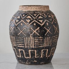 a black vase with designs on it sitting on a table next to a white wall