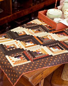 a quilted table runner sitting on top of a wooden table next to plates and cups