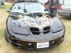 a man standing next to a black sports car with flames on it's hood