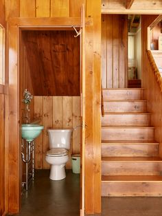 a bathroom with wooden walls and stairs leading to the upper floor, along with a toilet and sink