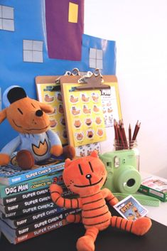 stuffed animals and books on a desk in front of a bulletin board with stickers