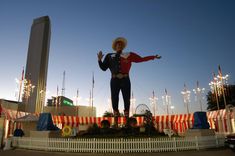 a large statue of a man wearing a cowboy hat and holding his arms out in the air