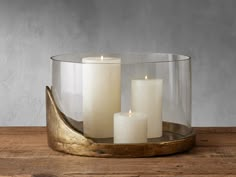 three white candles sitting in a glass container on a wooden table next to another candle