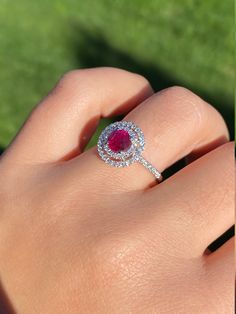 The Titania Double Halo Ruby and Diamond Ring in 14 Karat White Gold. This contemporary cocktail ring centers on a 1.05 carat ruby. The ruby is encircled by a double diamond halo with diamonds continuing down either side of the shank. The mounting has 0.58 total carats of diamonds. This modern ring is a finger size 6 3/4, yet can be adjusted to any size. Each piece has been hand selected and meticulously identified and graded by a Graduate Gemologist who has been awarded a degree by the Gemologi Gia Certified Round Cut Ruby Ring Fine Jewelry, Ruby Ring With Brilliant Cut Diamond, Brilliant Cut Diamond Ruby Ring, Gia Certified Round Cut Ruby Ring, Round Brilliant Cut Ruby Ring With Diamonds, Brilliant Cut Ruby Ring With Diamonds, Gia Certified Ruby Ring, Dazzling Gia Certified Ruby Ring, Gia Certified Diamond Ruby Ring For Anniversary