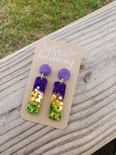 purple, green and yellow earrings on top of a piece of wood next to a tag