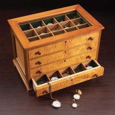 a wooden jewelry box with several compartments and two watch faces on the inside, one drawer open