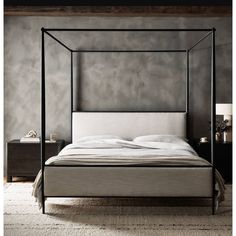 a four poster bed with white linens in a gray bedroom, next to a nightstand and night stand