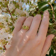 a woman's hand with a yellow gold ring on top of it and white flowers in the background