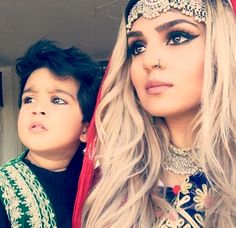 a woman with long blonde hair standing next to a little boy wearing a headdress