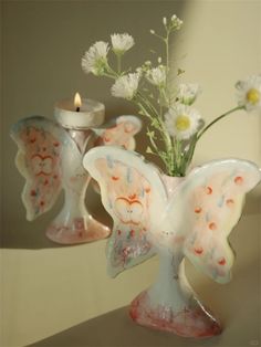 two glass angel figurines sitting next to a vase with daisies in it