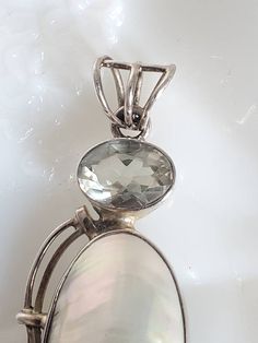 Vintage sterling silver mother of pearl and green amethyst pendant in excellent condition. This beautiful pendant features a bezel set oval large mother of pearl stone with a bezel set faceted pale green amethyst at the top. It measures 2 5/8" long (including bail) and 1" wide. Stamped "925." Nice swirl silver design on one side makes it unique. Large size bail will accommodate most chains (chain not included). Please see the additional photos. Oval Mother Of Pearl Gemstone Jewelry, Oval Mother Of Pearl Jewelry With Polished Finish, Oval Mother Of Pearl Necklace, Silver Oval Mother Of Pearl Jewelry, Silver Jewelry With Cabochon Mother Of Pearl, Oval Mother Of Pearl Silver Jewelry, Oval Silver Mother Of Pearl Jewelry, Oval Mother Of Pearl Jewelry For Anniversary, Mother Of Pearl Silver Jewelry For Mother's Day