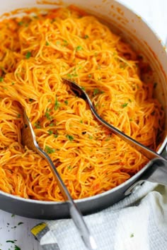 a pan filled with spaghetti and two serving spoons on top of the dish, ready to be eaten