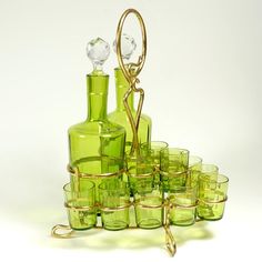 green glass bottles and glasses are arranged in a pyramid on a white background with gold trimmings