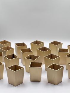 many square vases are lined up on a white surface, one is gold and the other is brown