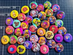 a pile of cartoon character buttons sitting on top of a blue table next to a ruler