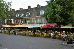 many people are sitting at tables with umbrellas in front of some buildings and trees