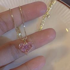 a person's hand holding a necklace with a heart shaped pink diamond on it