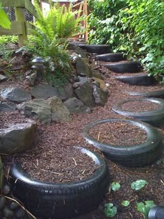 there are many tires lined up on the ground next to some rocks and plants in this garden